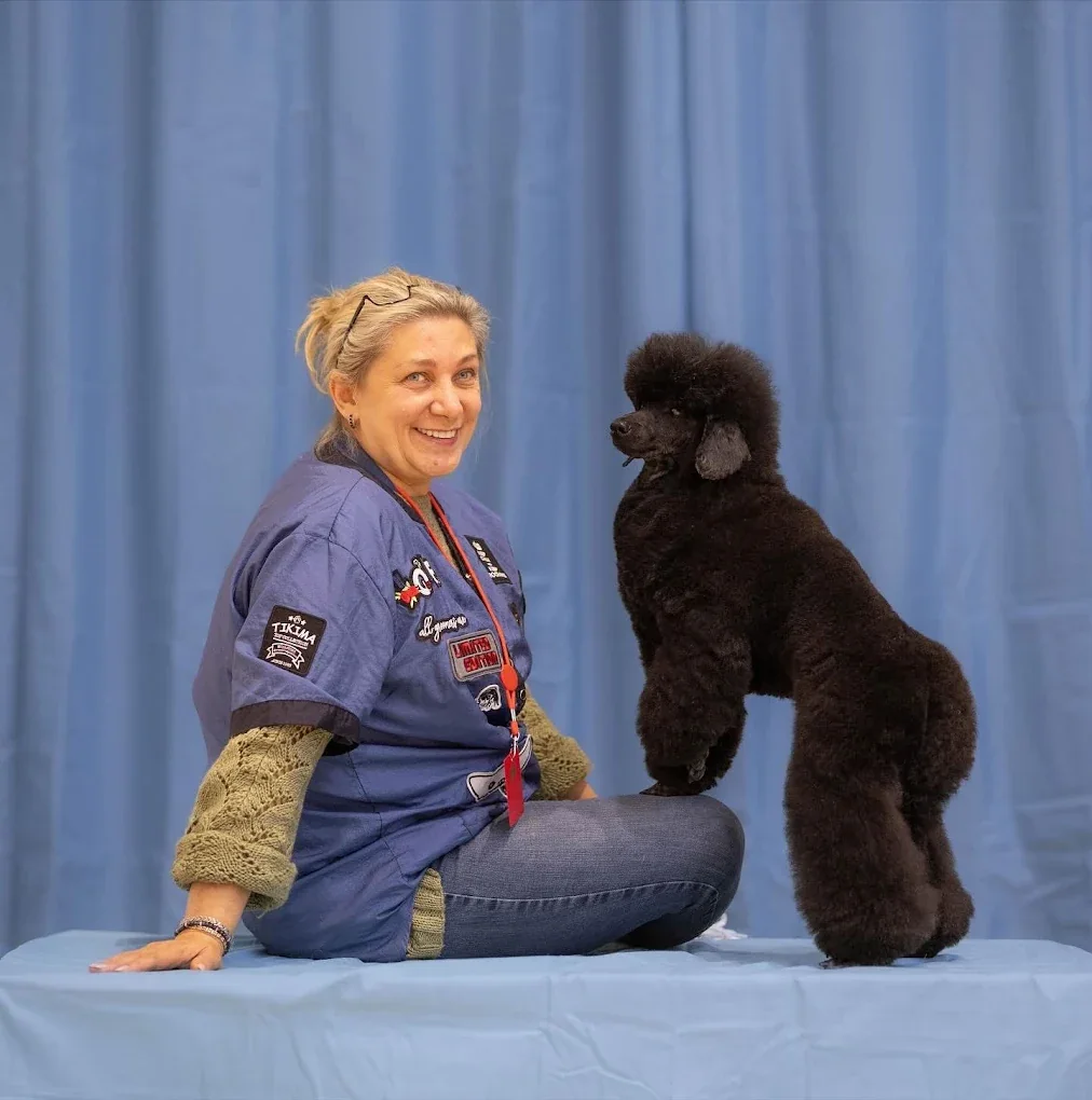 Sweet Paws groomer posing with a beautifully styled black poodle